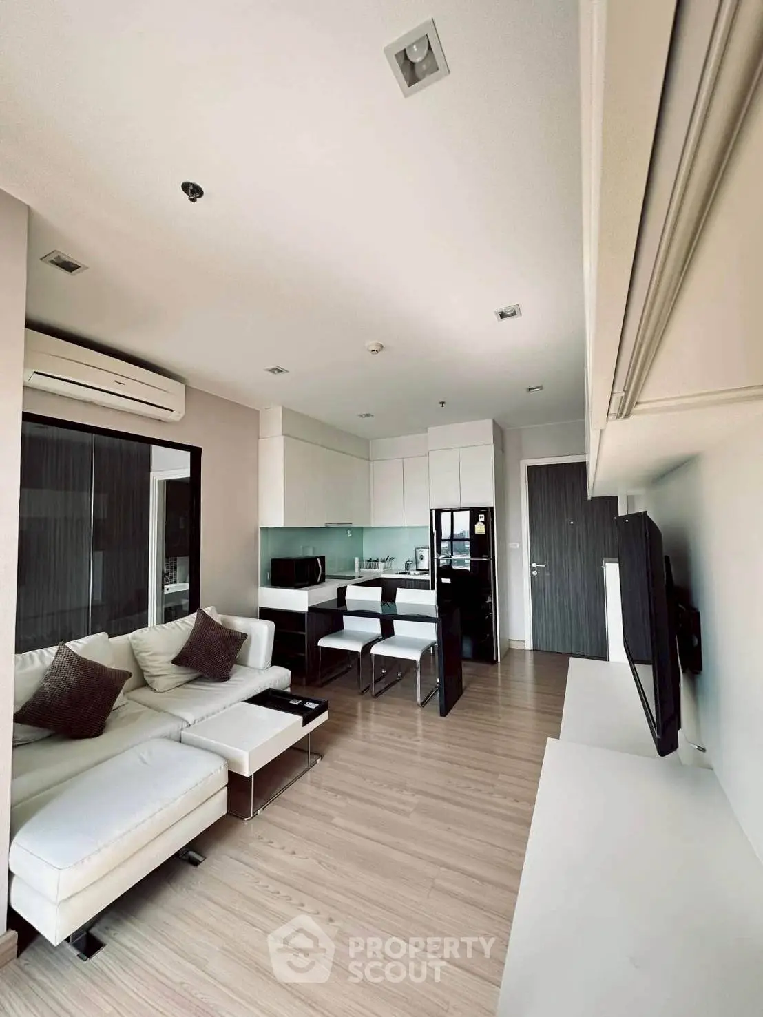 Modern open-layout living room with sleek kitchen, featuring white furniture and wooden flooring.