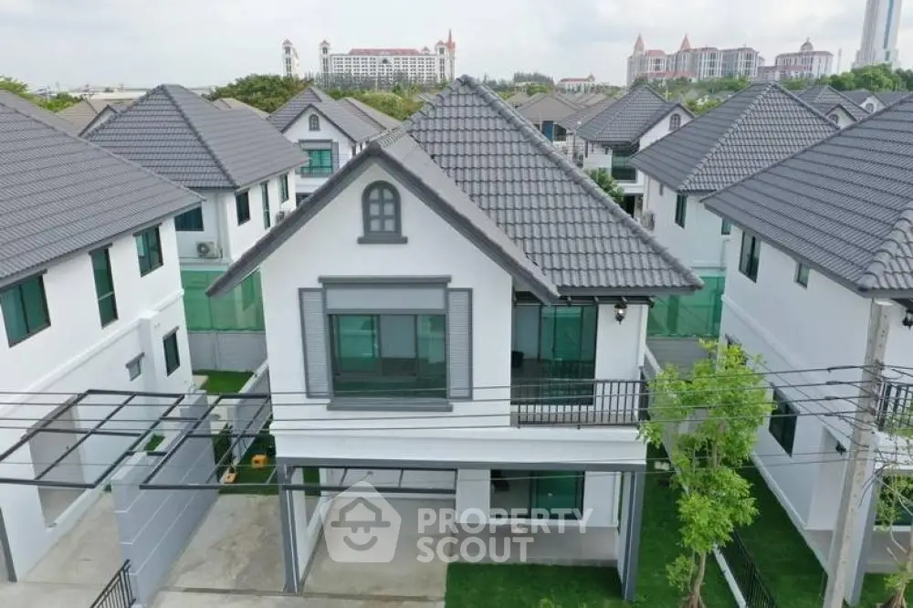 Elegant two-story house with a gray gable roof and a charming balcony, nestled in a peaceful suburban neighborhood with lush greenery.