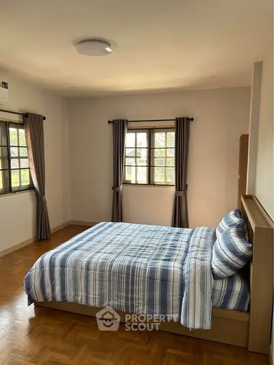 Spacious bedroom with cozy bedding and natural light from two windows.
