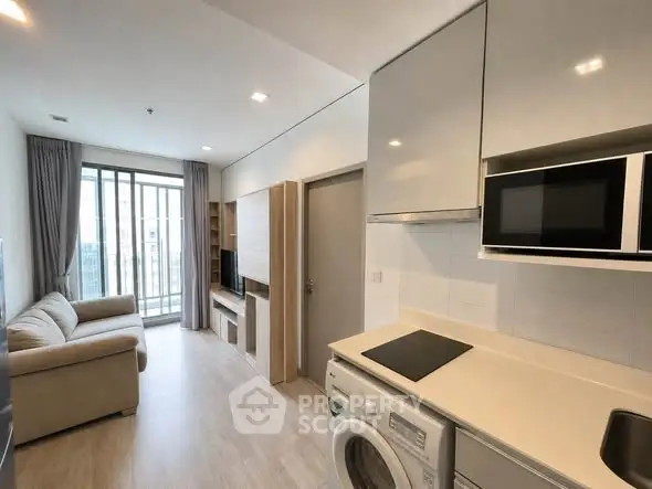 Modern open-plan living room and kitchen with sleek appliances and large windows.