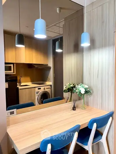Modern kitchen with dining area, featuring wooden cabinetry, washing machine, and stylish pendant lights.