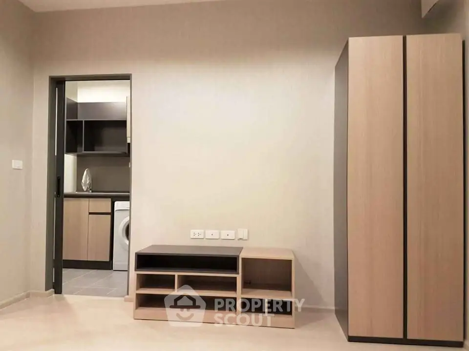 Modern apartment interior with sleek storage and view into kitchen with washing machine.