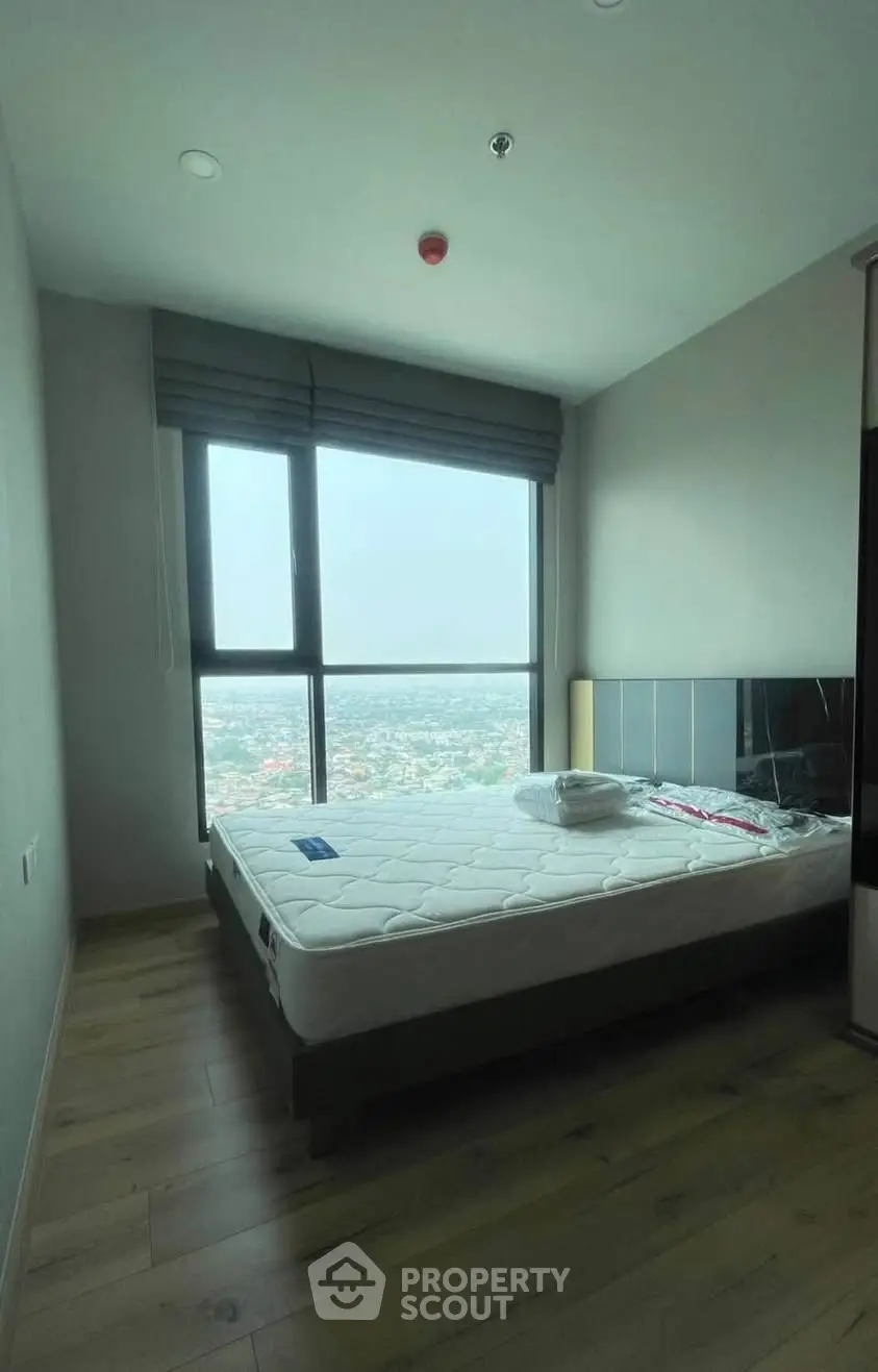 Cozy bedroom with large window offering stunning city view, perfect for relaxation and comfort.