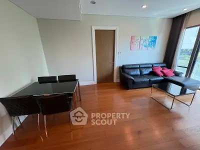 Modern living room with sleek black leather sofa and glass dining table, featuring elegant wooden flooring.