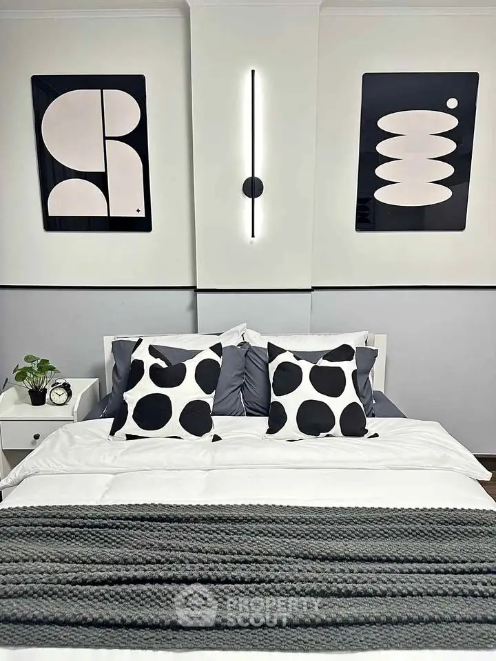 Modern bedroom with stylish decor and abstract art, featuring a cozy bed and elegant lighting.