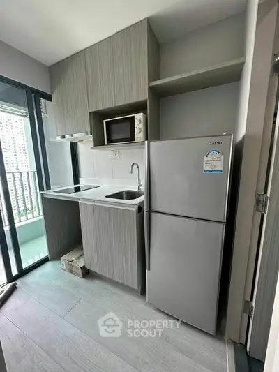 Modern compact kitchen with sleek cabinetry and balcony view in urban apartment.
