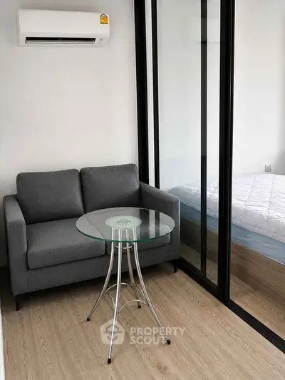 Modern studio apartment with glass partition, cozy sofa, and sleek glass table.