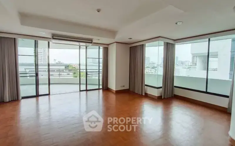 Spacious corner unit living room with large windows and balcony view in modern apartment.