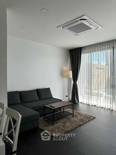 Modern living room with sleek furniture and large window offering natural light.