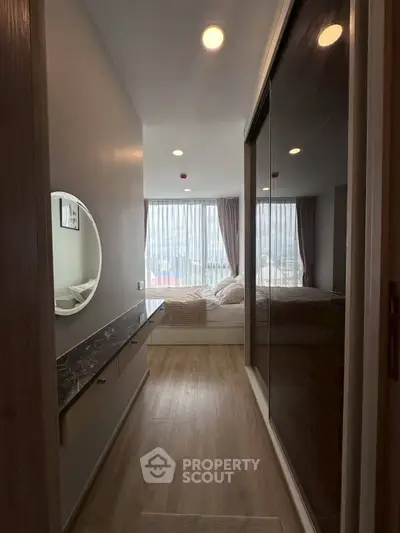 Cozy bedroom with large windows and modern decor, featuring a stylish round mirror and sleek wooden flooring.