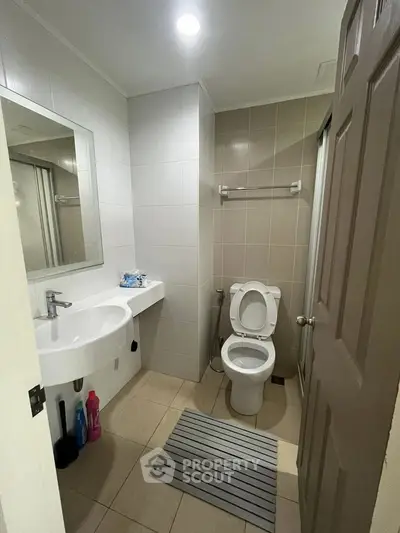 Modern bathroom with sleek fixtures and neutral tiles, featuring a toilet, sink, and shower area.