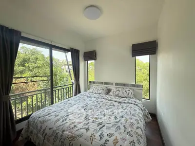 Bright bedroom with large windows and lush green views, featuring a cozy bed and elegant decor.