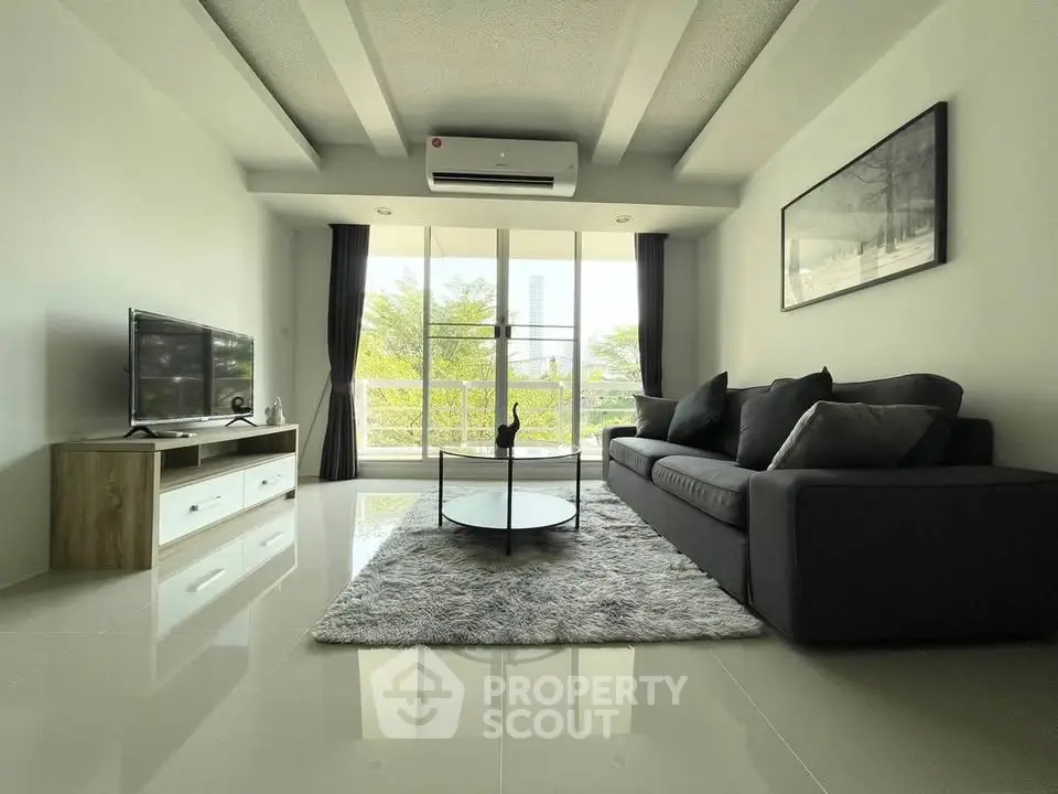 Modern living room with sleek furniture and large windows offering natural light and greenery views.