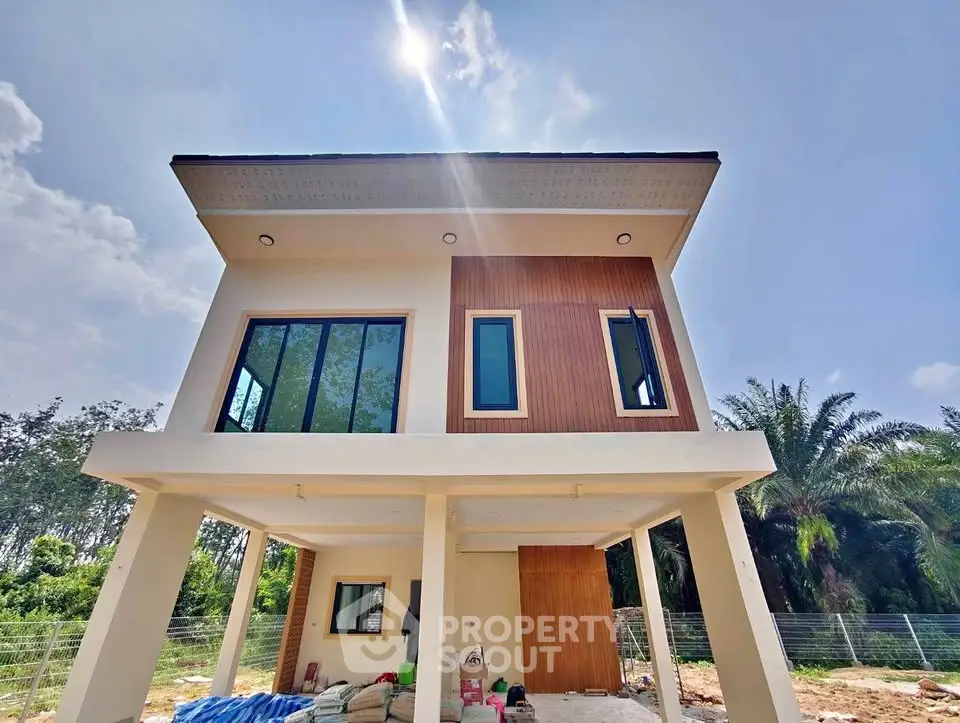 Modern two-story house with large windows and elevated design in a lush green setting.