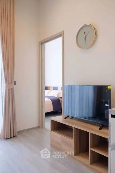 Modern living room with sleek TV stand and wall clock, leading to a cozy bedroom with soft lighting.