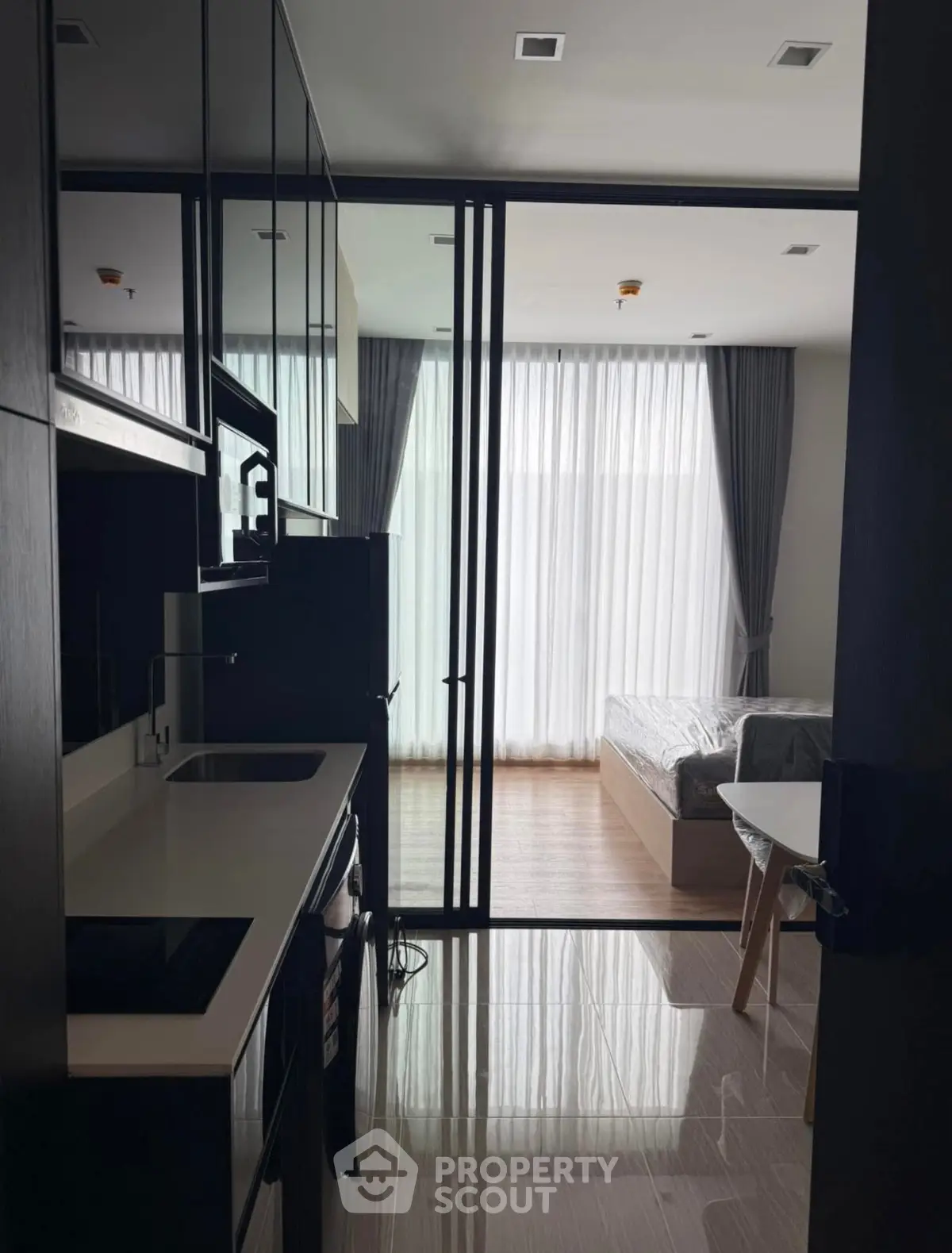 Modern studio apartment with sleek kitchen and cozy bedroom, featuring floor-to-ceiling windows and elegant decor.