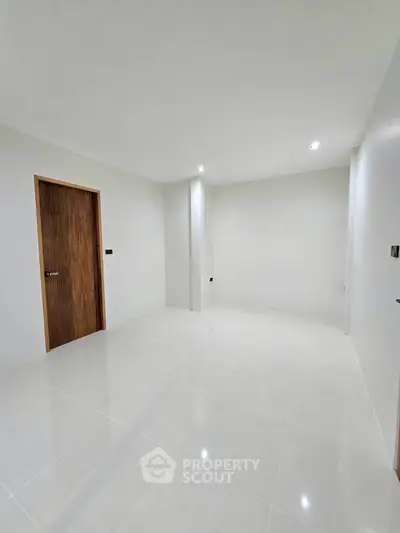Spacious minimalist room with sleek white tiles and wooden door, perfect for modern living.