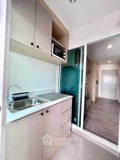 Modern compact kitchen with sleek cabinetry and built-in microwave in a stylish apartment.