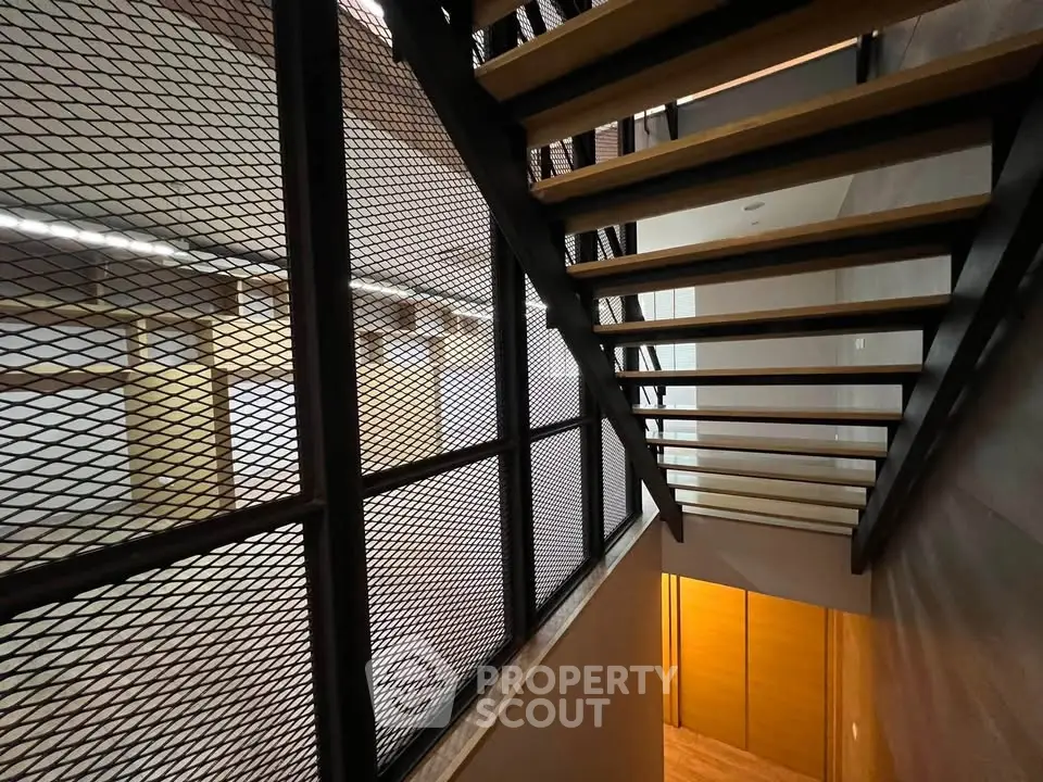 Modern industrial staircase with metal mesh railing and wooden steps in a contemporary building.