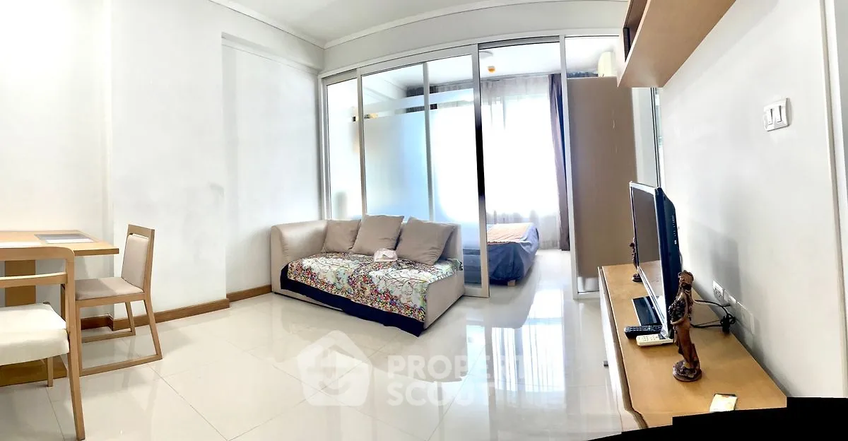 Modern living room with cozy sofa and TV, adjacent to a bright bedroom with large windows.