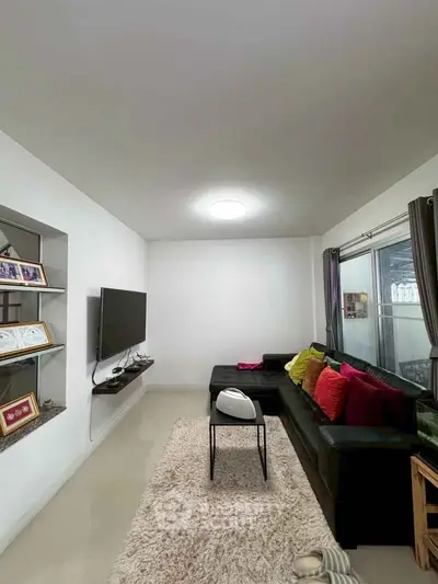 Modern living room with sleek TV setup and colorful cushions on a cozy sofa.