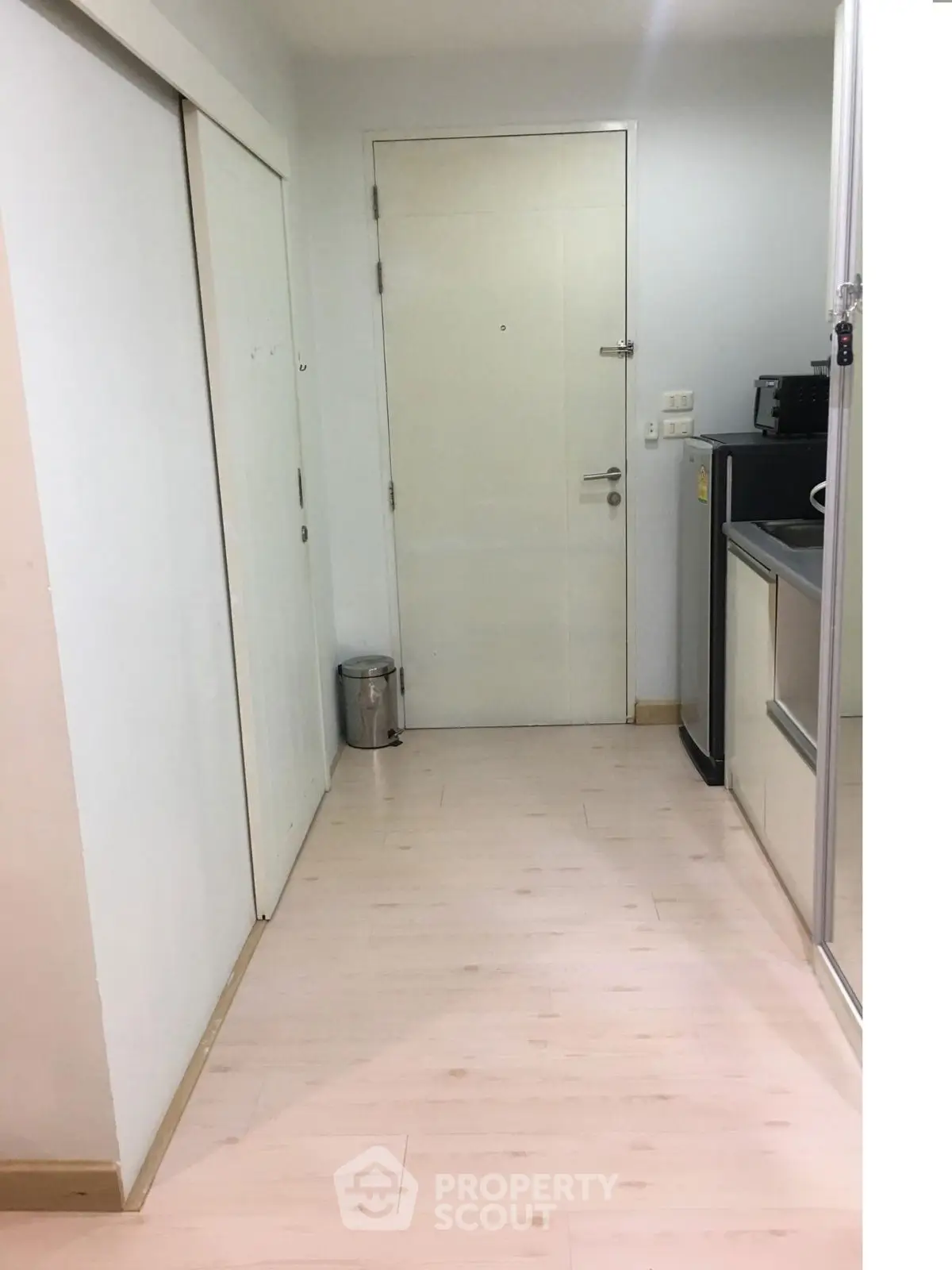 Modern apartment entrance with sleek kitchen area and light wood flooring.