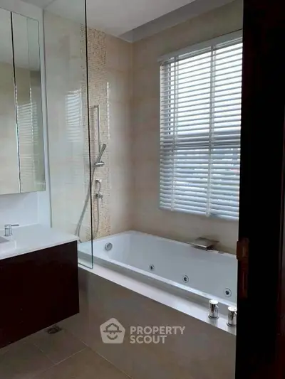 Modern bathroom with sleek bathtub and large window with blinds.