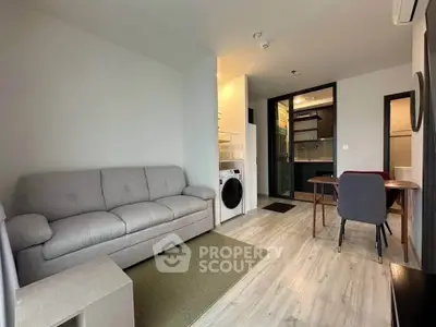 Modern living room with cozy sofa, dining area, and in-unit washer in a compact apartment.