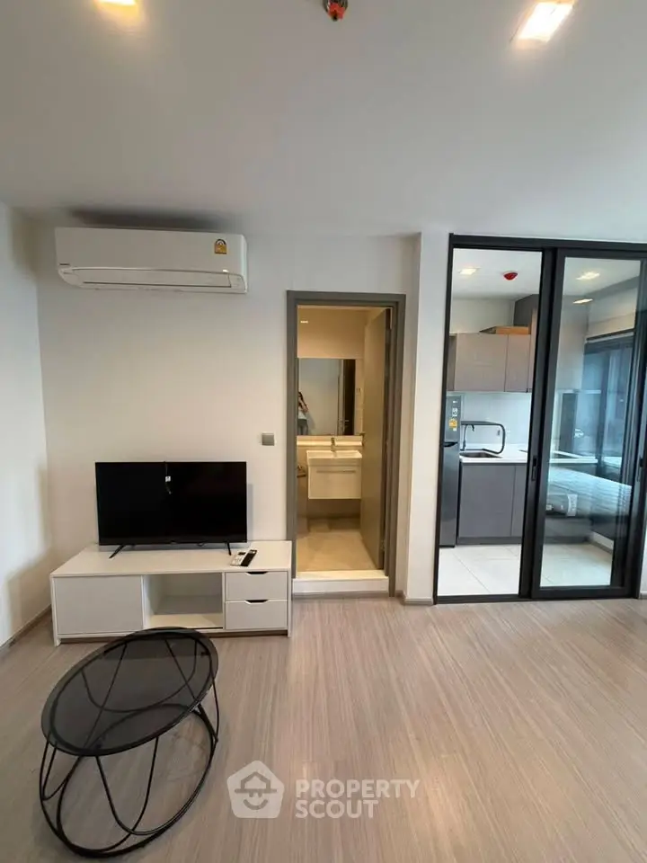 Modern living room with sleek design, featuring air conditioning, TV, and open kitchen layout.