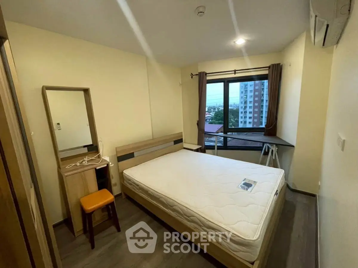 Spacious bedroom with large window offering city views, featuring modern furniture and air conditioning.