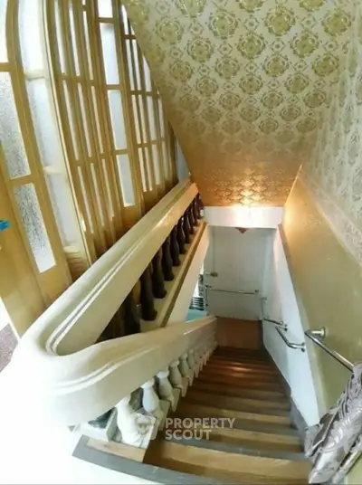 Elegant staircase with ornate railing and patterned wallpaper in a luxurious home.