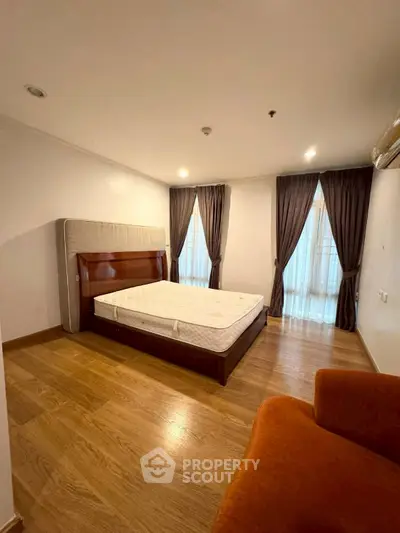 Spacious bedroom with wooden flooring and large windows for natural light