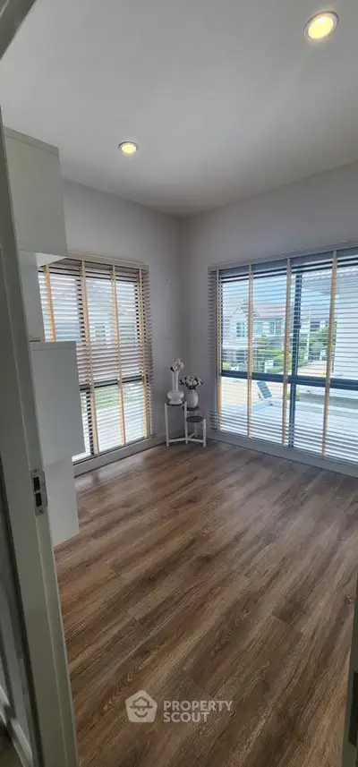Bright room with large windows and wooden flooring, perfect for a cozy living space.