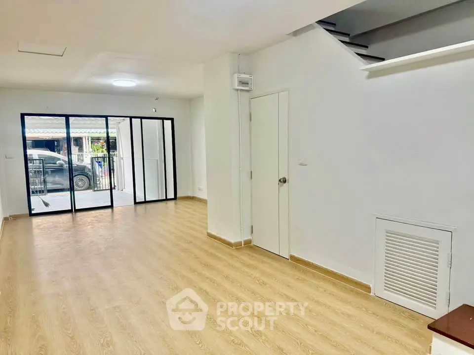 Spacious modern living room with wooden flooring and large glass doors leading to a balcony.