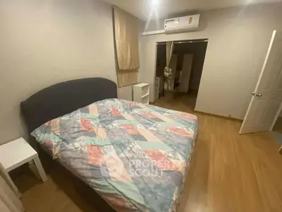 Cozy bedroom with wooden flooring and air conditioning, featuring a colorful bedspread.