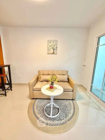 Cozy living room with beige sofa and round table, perfect for relaxation.