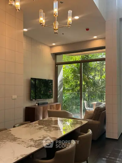 Luxurious living room with modern decor and lush garden view, featuring elegant chandelier and marble dining table.