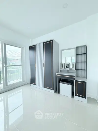 Spacious bedroom with modern wardrobe and vanity set, featuring large windows for natural light.