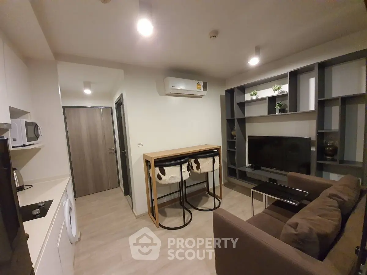 Modern living room with stylish furniture and built-in shelving, featuring a compact kitchen area.