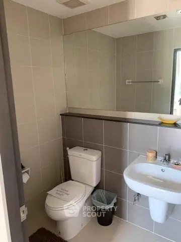 Modern bathroom with sleek fixtures and neutral tiles, featuring a wall-mounted sink and a large mirror.