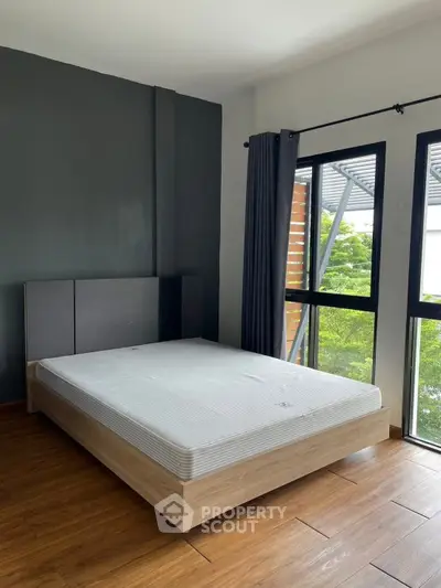 Modern bedroom with large windows and wooden flooring, offering a serene and bright atmosphere.