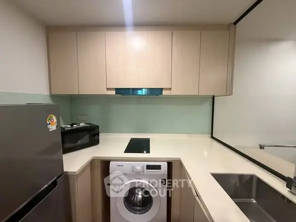 Modern kitchen with washing machine, fridge, and sleek cabinetry in compact layout.