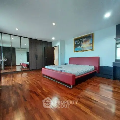 Spacious bedroom with hardwood floors and modern red bed frame