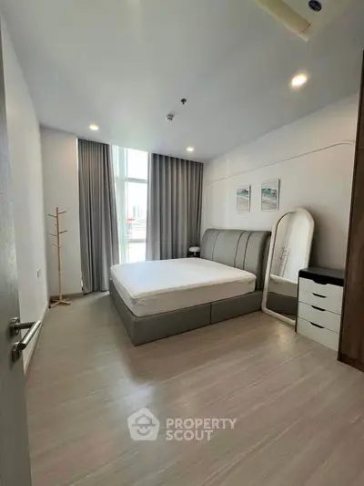 Spacious modern bedroom with sleek furniture and large window offering natural light.