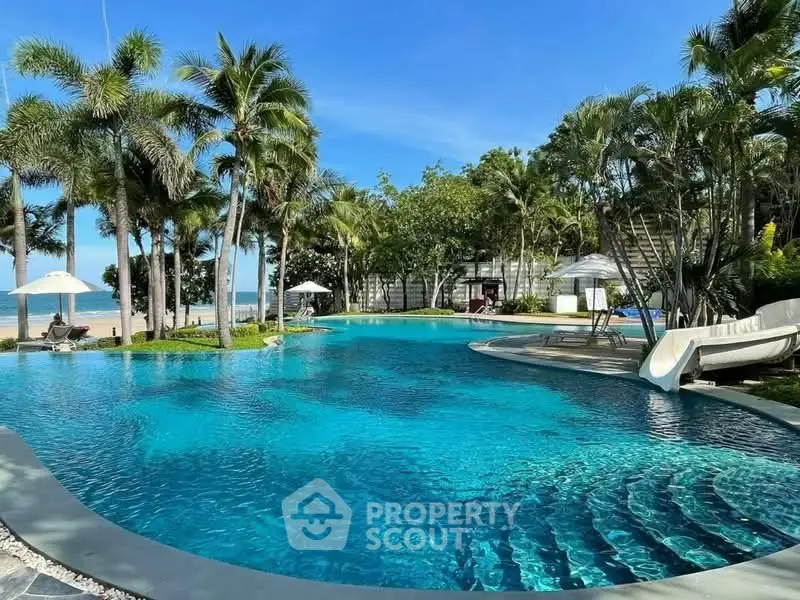 Luxurious resort-style pool with palm trees and ocean view, perfect for relaxation and leisure.
