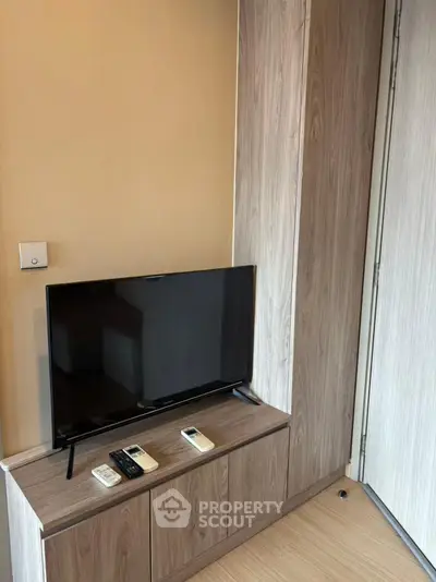 Modern living room with sleek TV stand and flat-screen TV, showcasing minimalist design and warm wood tones.