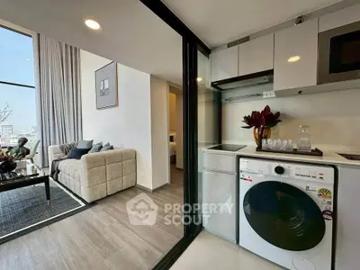 Modern apartment with open layout, featuring a cozy living room and compact kitchen with washing machine.