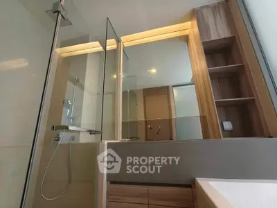 Modern bathroom with glass shower and wooden cabinetry in sleek apartment.
