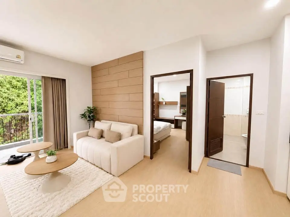Modern open-plan living room with cozy sofa, wooden accents, and view of bedroom and bathroom.