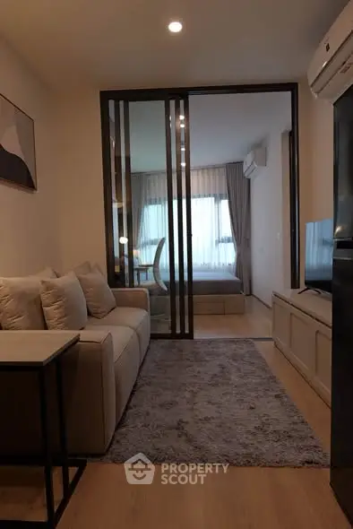 Modern living room with cozy sofa and view into stylish bedroom through glass doors.